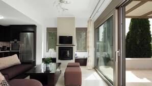 A modern living room with a sofa, coffee table, and a fireplace. There is a television mounted above the fireplace and a sliding glass door leading to an outdoor area. - Charming 2-Bedroom Villa in Serene Village - Perfect Family Getaway (Rethymno)