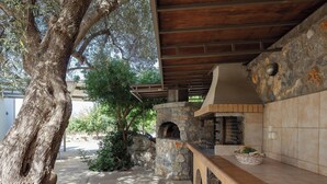 An outdoor kitchen area with a stone oven, wooden counter, and a large tree providing shade. - Charming 2-Bedroom Villa in Serene Village - Perfect Family Getaway (Rethymno)