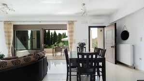 A modern living room with a glass dining table, dark wooden chairs, and a sofa with patterned cushions. - Charming 2-Bedroom Villa in Serene Village - Perfect Family Getaway (Rethymno)