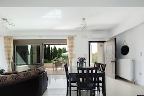 Ein modernes Wohnzimmer mit einem Glastisch, dunklen Holzstühlen und einem Sofa mit gemusterten Kissen.
