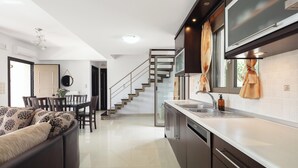 A modern kitchen with a built-in oven, a dining area with a glass-top table, and a staircase leading to another level. - Charming 2-Bedroom Villa in Serene Village - Perfect Family Getaway (Rethymno)