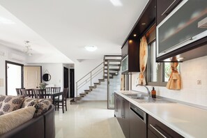 Eine moderne Küche mit Einbauofen, ein Essbereich mit Glastisch und eine Treppe, die zu einer anderen Ebene führt.