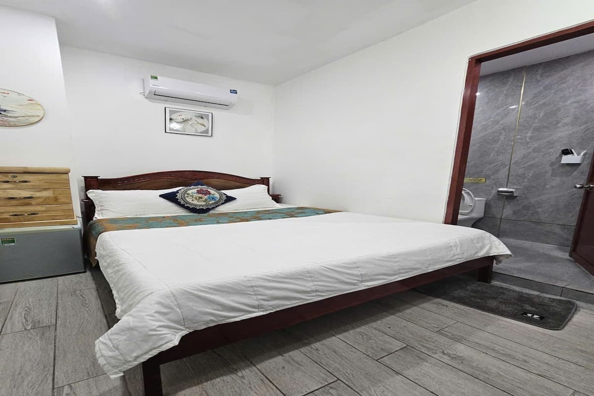 Hotelkamer met een bed, een houten dressoir, een airconditioner, een douche en een deur met marmeren afwerking.