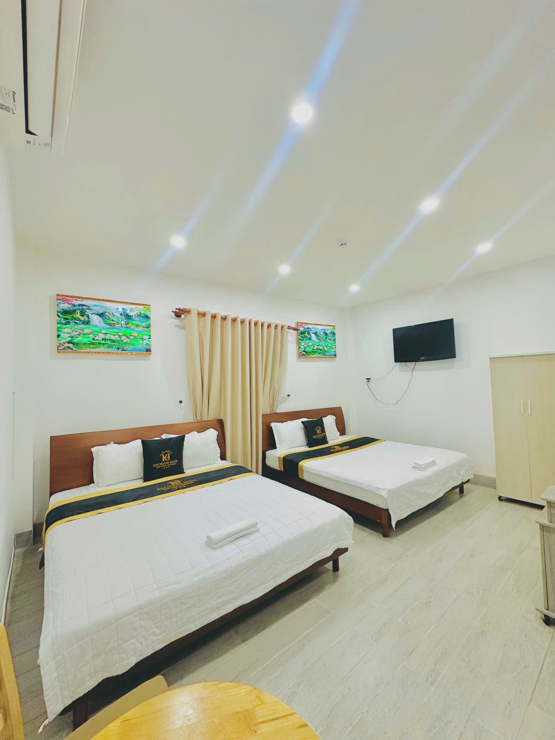 A hotel room with two beds, a TV, and artwork on the walls.