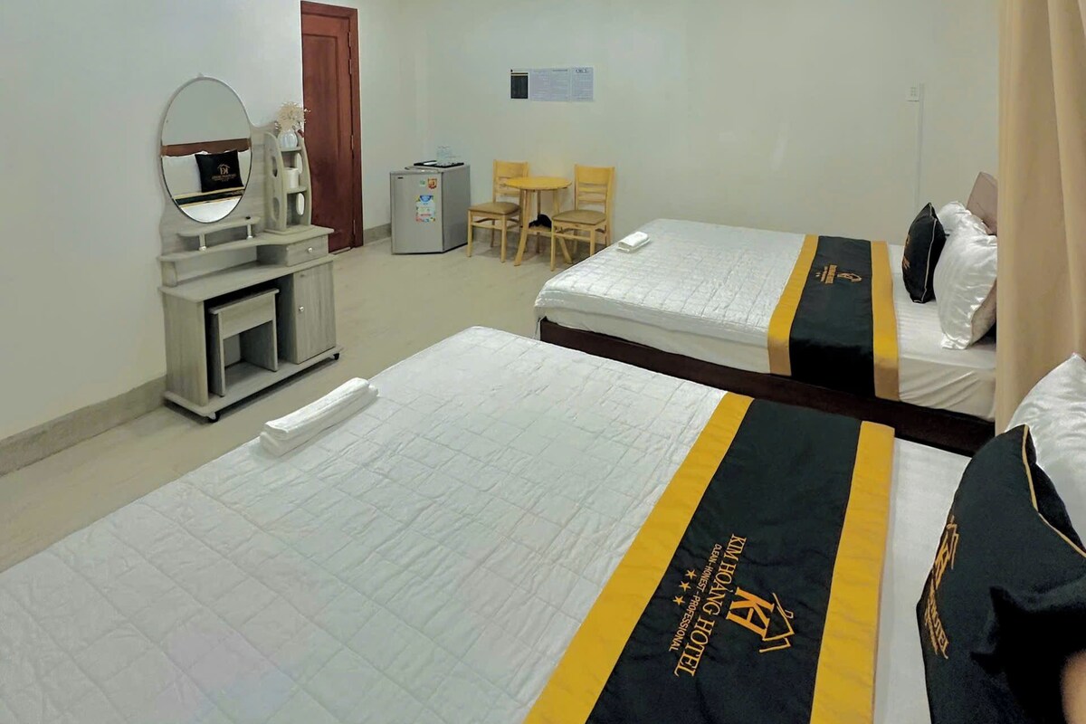 A hotel room with two beds, a desk with a mirror, a small refrigerator, and a chair.