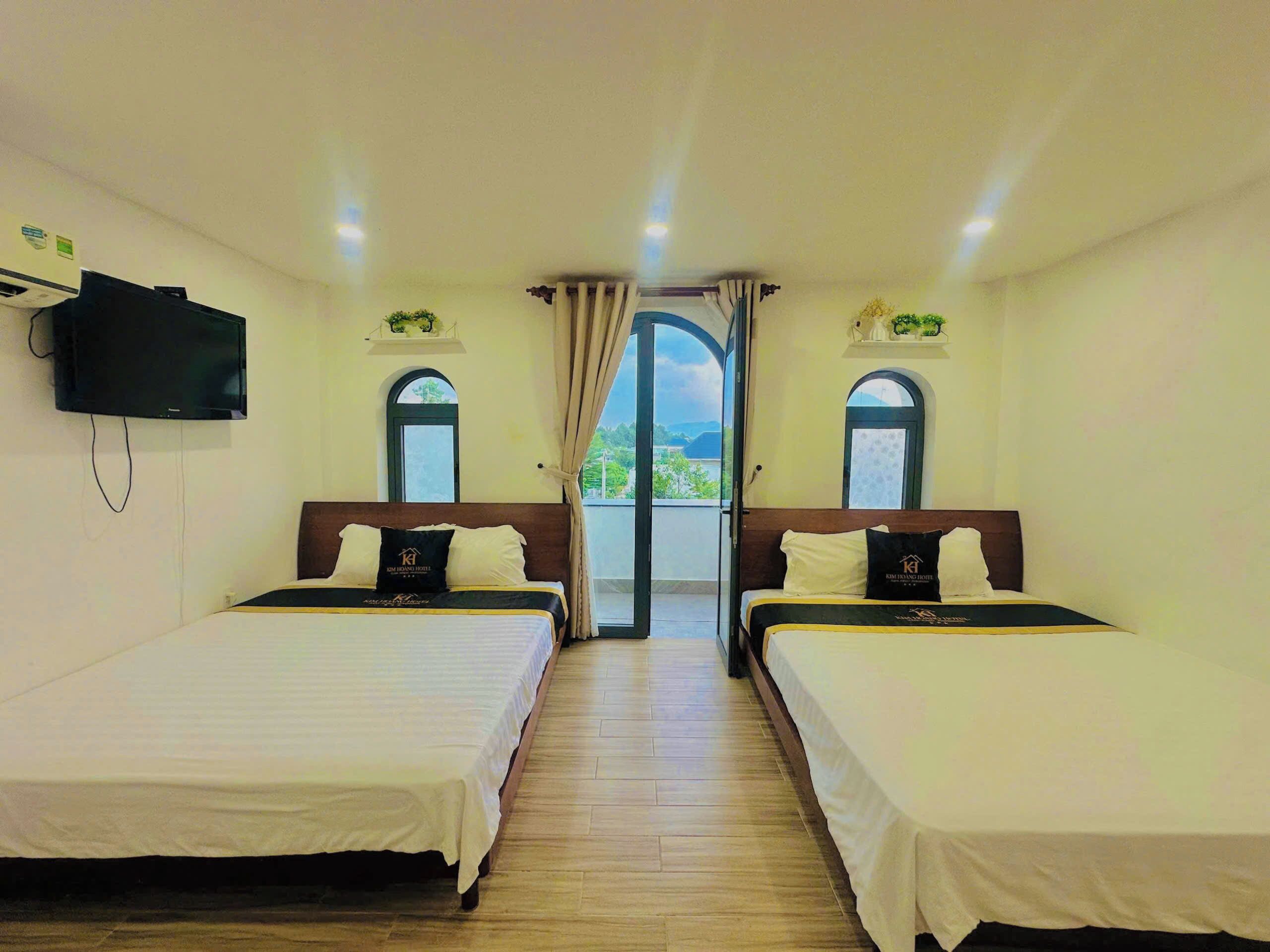 Quarto de hotel com duas camas, televisão e vista para o exterior.