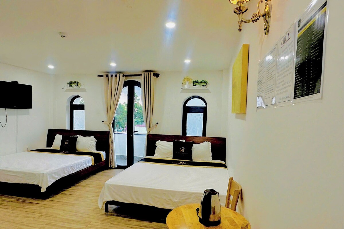 A hotel room with two beds, a wooden table with a kettle, and a television on the wall.