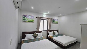 Habitación de hotel con dos camas, una ventana con cortinas y un aire acondicionado instalado en la pared.