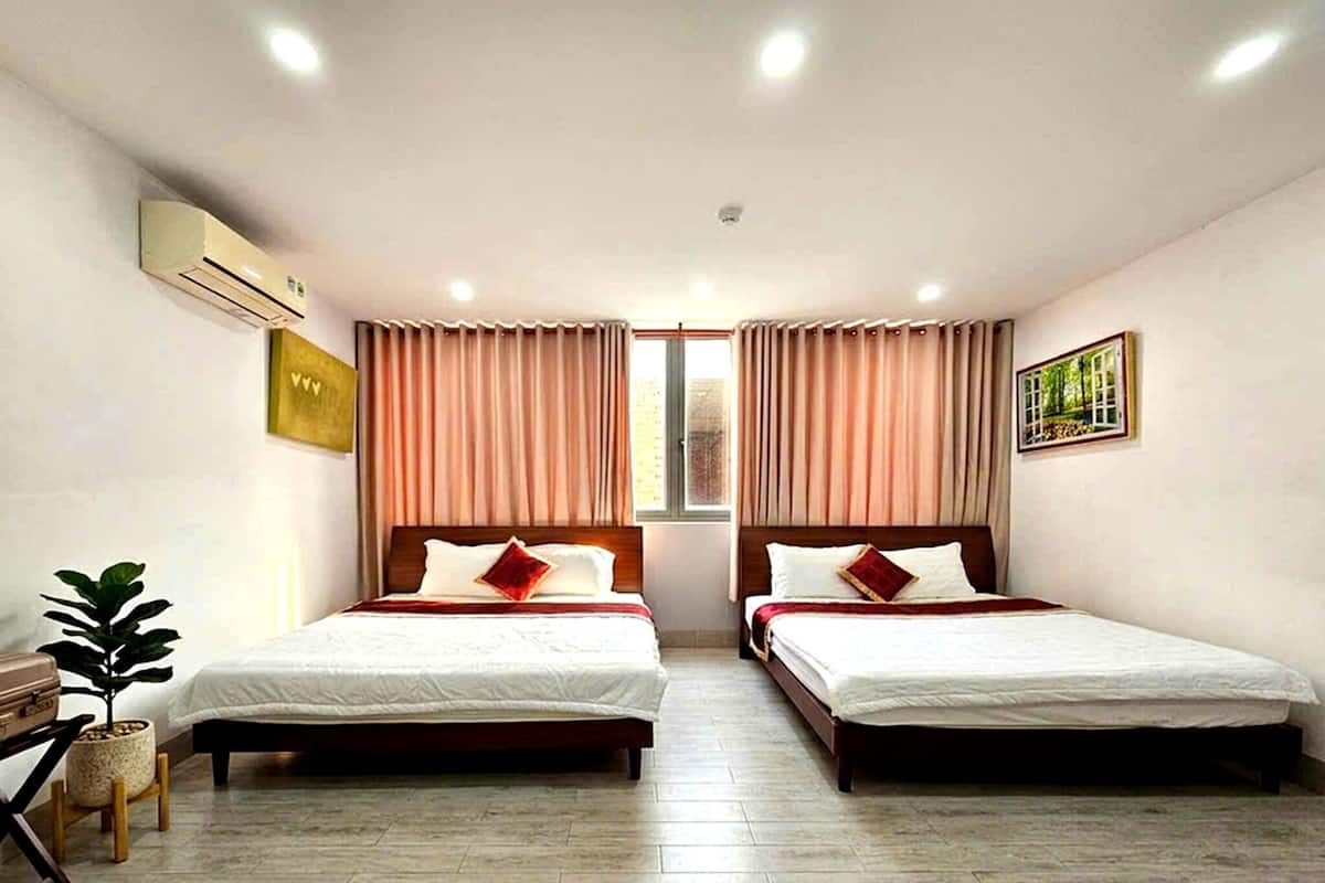 Een hotelkamer met twee bedden, een kamerplant, een airconditioner en een raam met gordijnen.