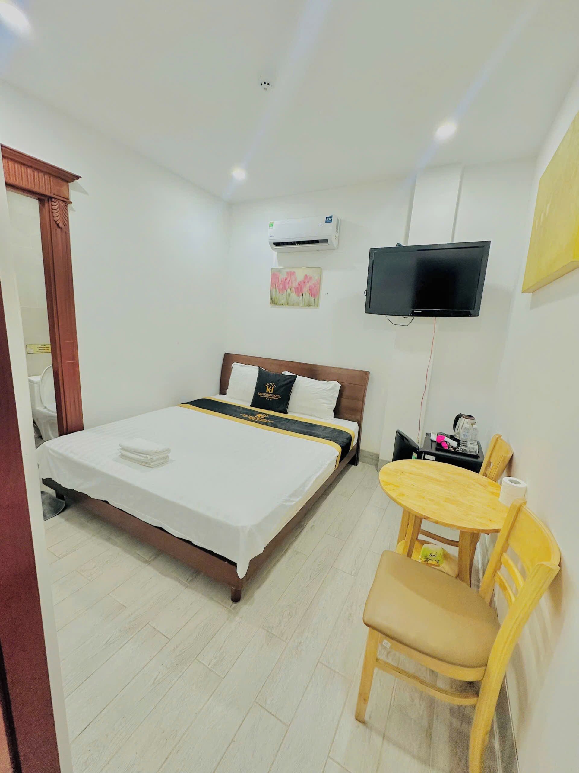 A hotel room with a bed, a desk, a chair, an air conditioner, and a TV.