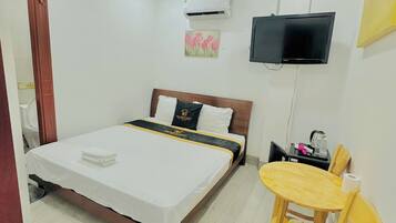 A hotel room with a bed, a desk, a chair, an air conditioner, and a TV.