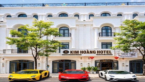 A hotel with a classic facade, three luxury cars parked in front, and a sign indicating it's the Kim Hoang Hotel. - KIM HOÀNG HOTEL TÂY NINH (Tan Ninh)