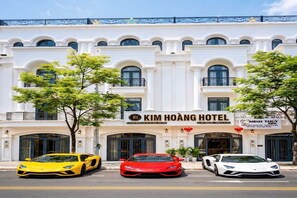 Un hôtel à la façade classique, avec trois voitures de luxe garées devant, et une enseigne indiquant qu’il s’agit de l’hôtel Kim Hoang.