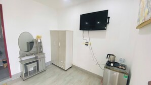Una habitación con televisión de pantalla plana en la pared, kitchenette con cafetera y armario.