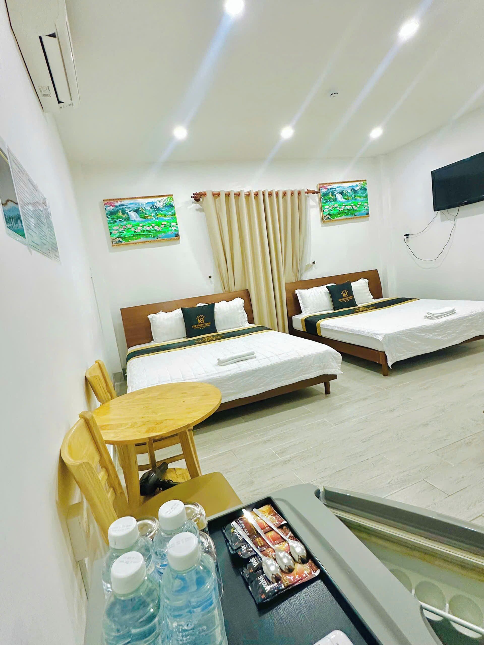 Habitación de hotel con dos camas, una mesita, sillas y un televisor en la pared.