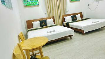 Habitación de hotel con dos camas, una mesita, sillas y un televisor en la pared.