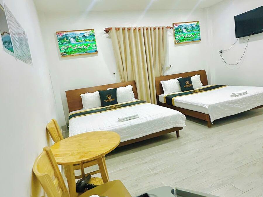 Habitación de hotel con dos camas, una mesita, sillas y un televisor en la pared.