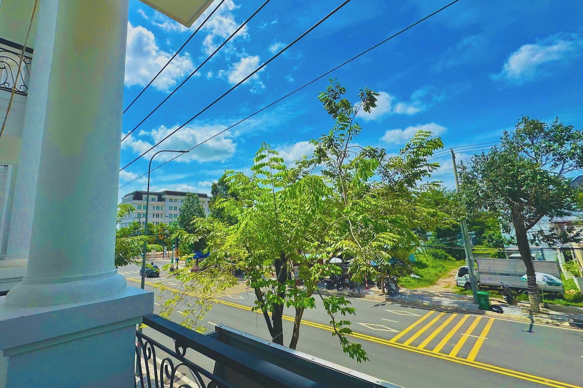 A balcony with a view of a street, trees, and a building in the background.