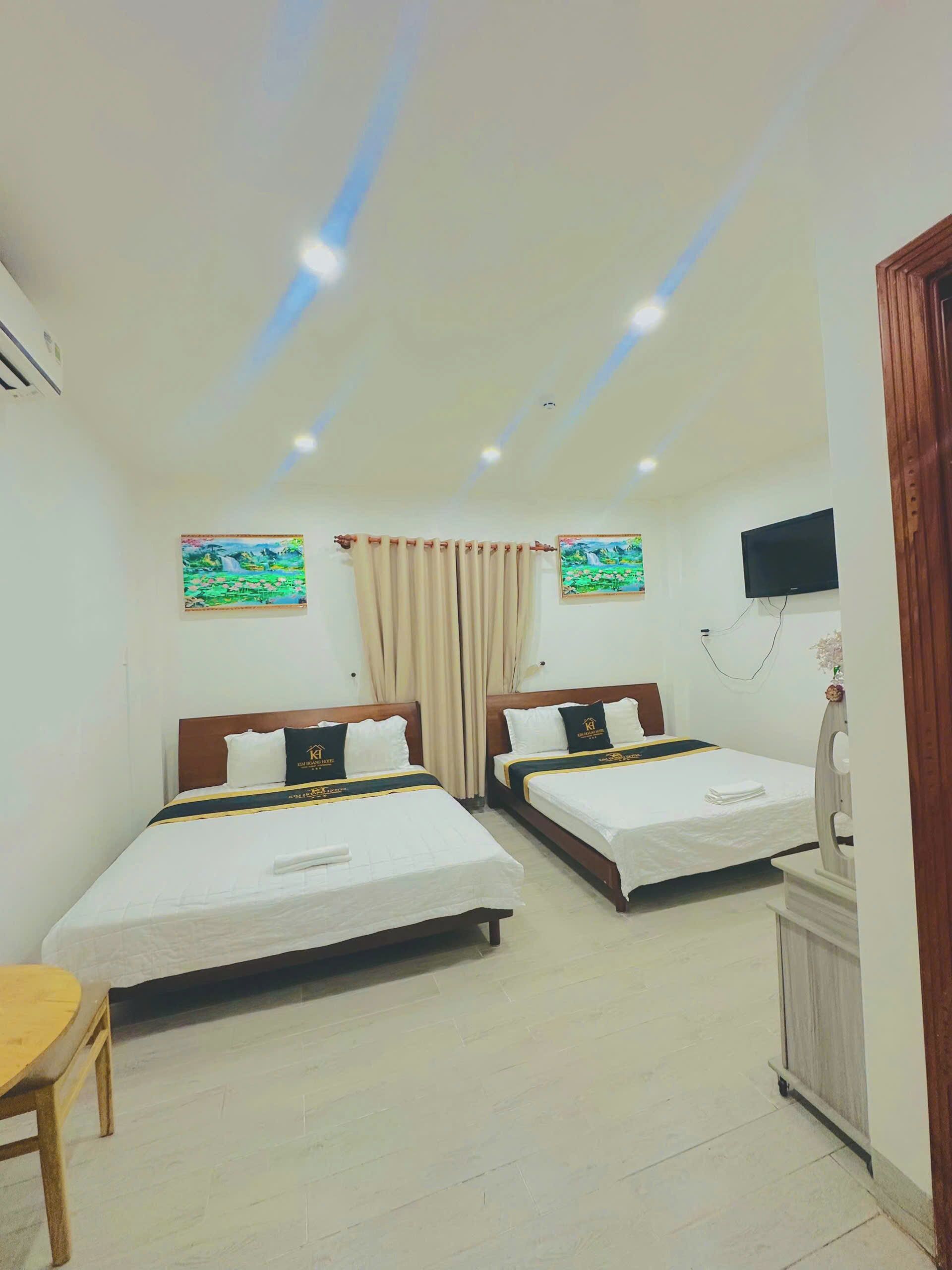 A hotel room with two beds, a TV, and artwork on the walls.