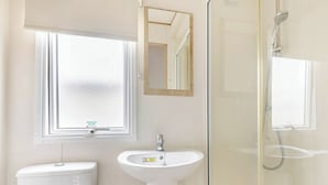 Et badeværelse med toilet, håndvask, spejl og bruser.