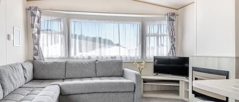 Una sala moderna con un sofá gris, un televisor de pantalla plana y una zona de comedor.