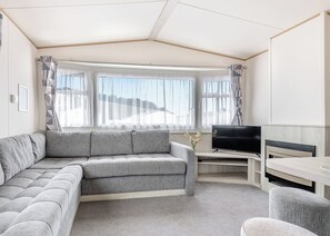 Ein modernes Wohnzimmer mit einem grauen Sofa, einem Flachbildfernseher und einem Essbereich.