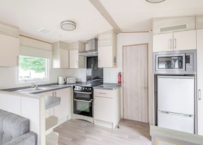 A compact kitchen with a built-in oven, a microwave, and a refrigerator. - Gold 4 Bedroom Caravan with parking and decking (Skegness)
