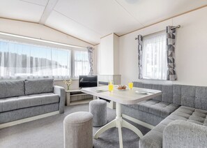 Interior moderno de una caravana con sofá, mesa, reposapiés y televisión.