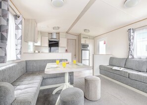 A modern RV interior with a dining area, kitchenette, and seating space. - Gold 4 Bedroom Caravan with parking and decking (Skegness)