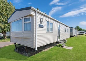 A mobile home with a flat roof, large windows, and a sign indicating 'Summer Breeze Deluxe.' - Gold 4 Bedroom Caravan with parking and decking (Skegness)
