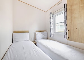 Un alojamiento pequeño y con una sola habitación, con dos camas, una ventana con cortinas y un panel de madera en una pared.