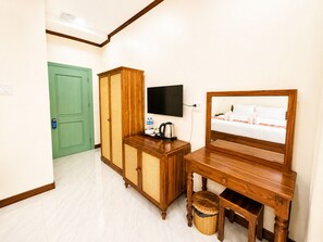 A hotel room with a bed, a television, a wooden cabinet, a wicker basket, and a green door. - Phousi Aphay Hotel (Luang Prabang)
