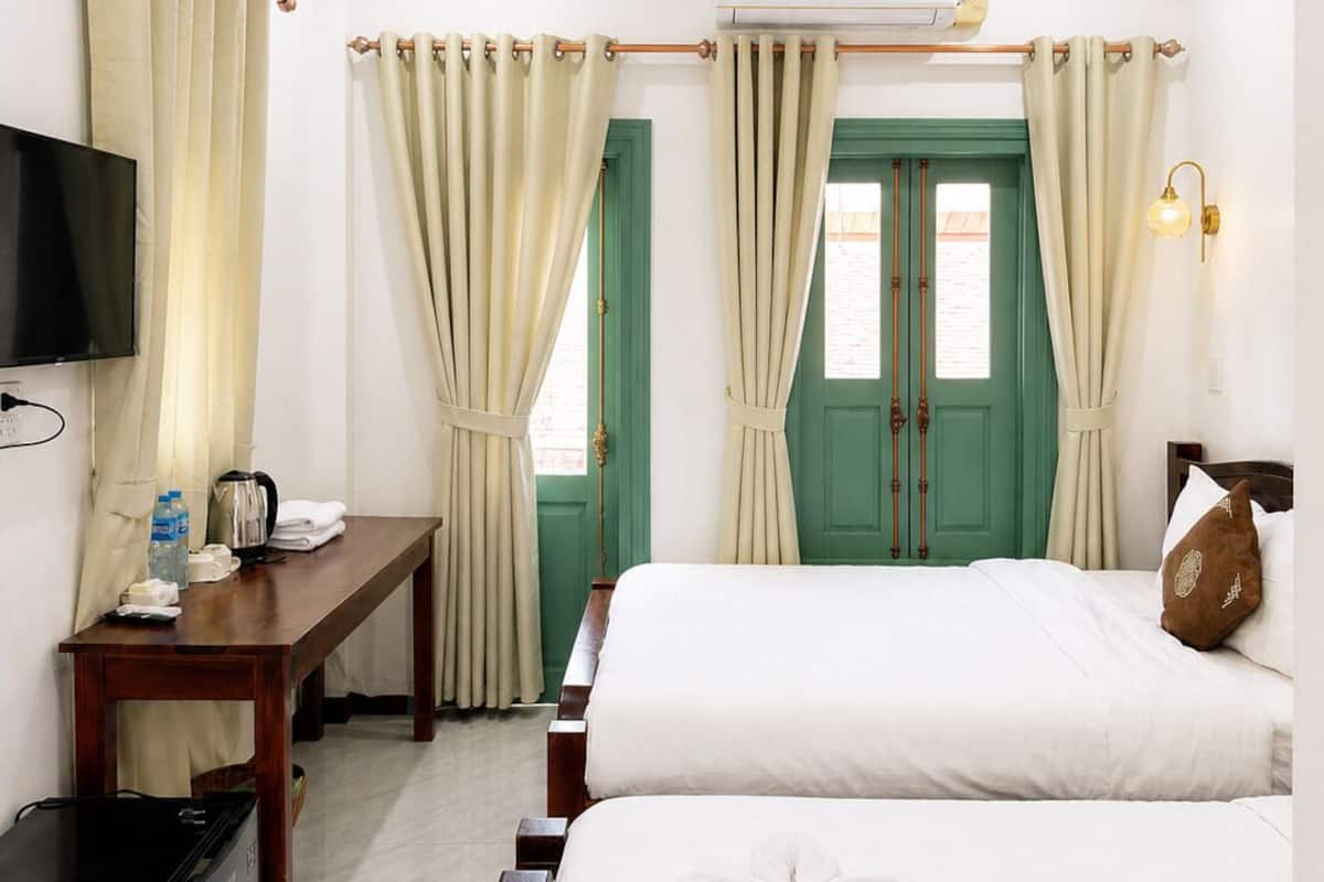 A hotel room with two beds, a desk, a television, an air conditioning unit, and a ceiling fan.