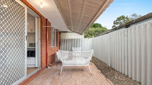 A patio with a white metal chair, a brick floor, and a corrugated metal fence. - Quiet Comfortable - A Sepal Stay (Perth)