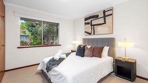 A bedroom with a bed, two bedside lamps, a window with a view, and a large abstract painting on the wall. - Quiet Comfortable - A Sepal Stay (Perth)