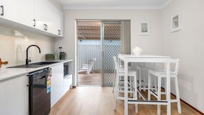 A modern kitchen with white cabinets, a dishwasher, and a dining area with a white table and chairs. - Quiet Comfortable - A Sepal Stay (Perth)