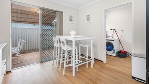 A compact room with a dining table and chairs, a washing machine, and a sliding glass door leading to an outdoor area. - Quiet Comfortable - A Sepal Stay (Perth)