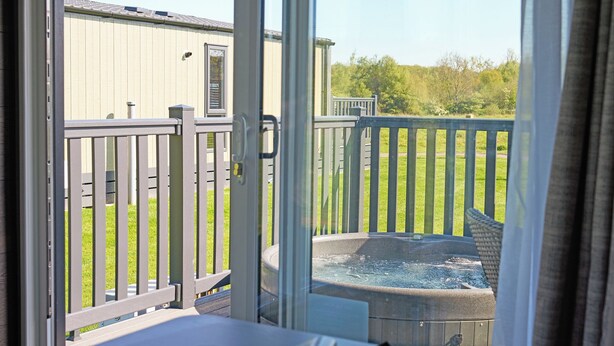 Ein Zimmer mit einer Schiebetür zu einem Balkon mit Whirlpool und Blick auf einen umzäunten Garten.