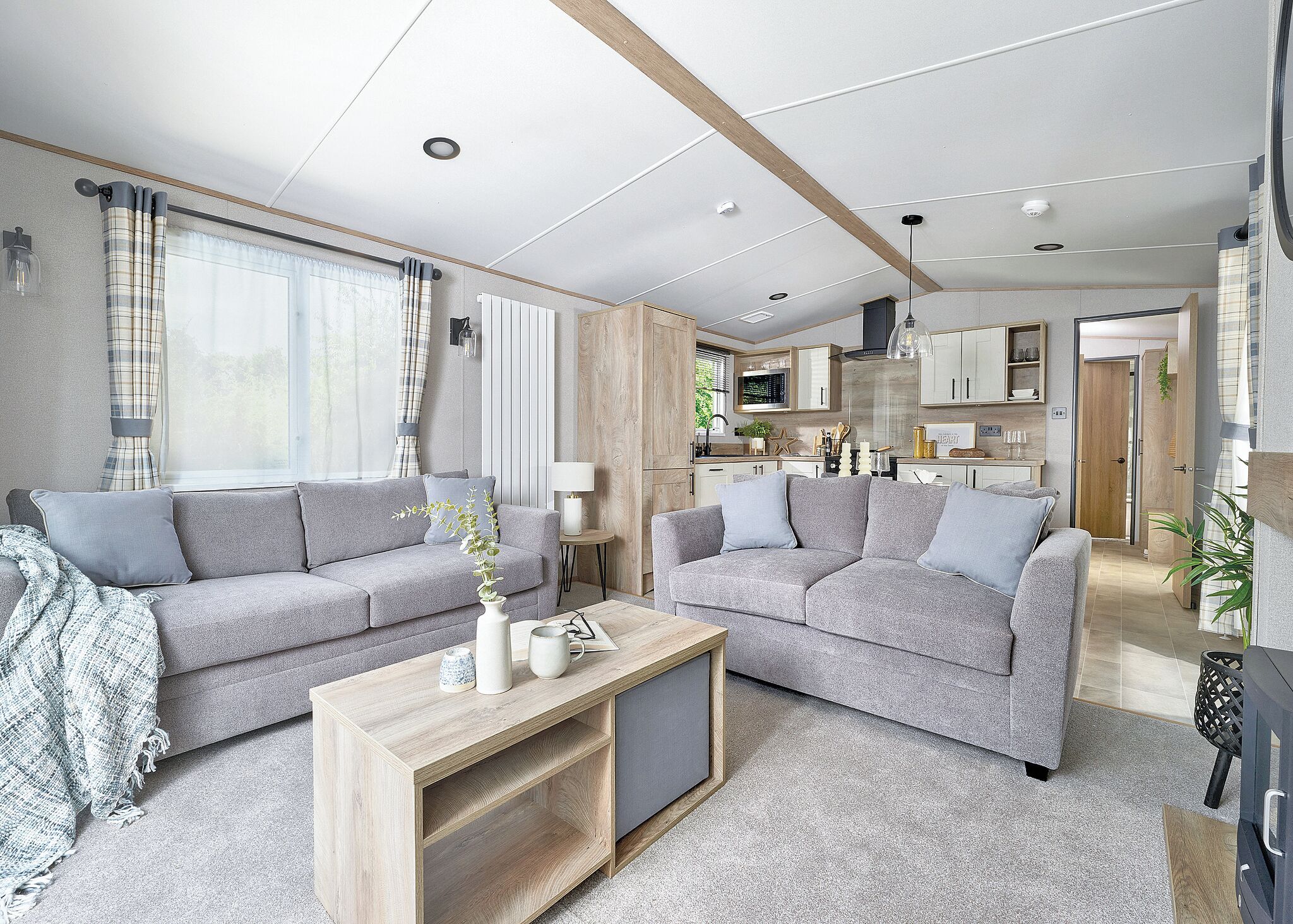 A modern living room with two grey sofas, a wooden coffee table, and a kitchen in the background.