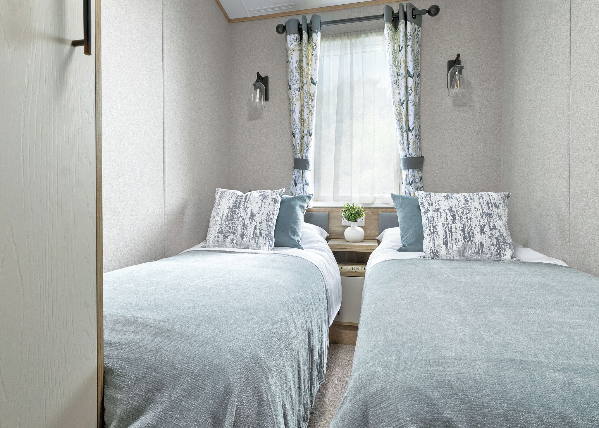 Ein Schlafzimmer mit zwei Betten, einem Nachttisch mit einer Vase und einem Fenster mit Vorhängen.