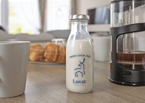 A bottle of fresh local milk, a white mug, and a coffee maker on a wooden table.