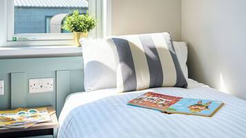 A bedroom with a bed, a window, a plant, and a book on the nightstand.