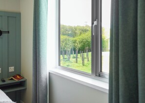 A room with a window, a bed, a bedside table with a book, and a power outlet.