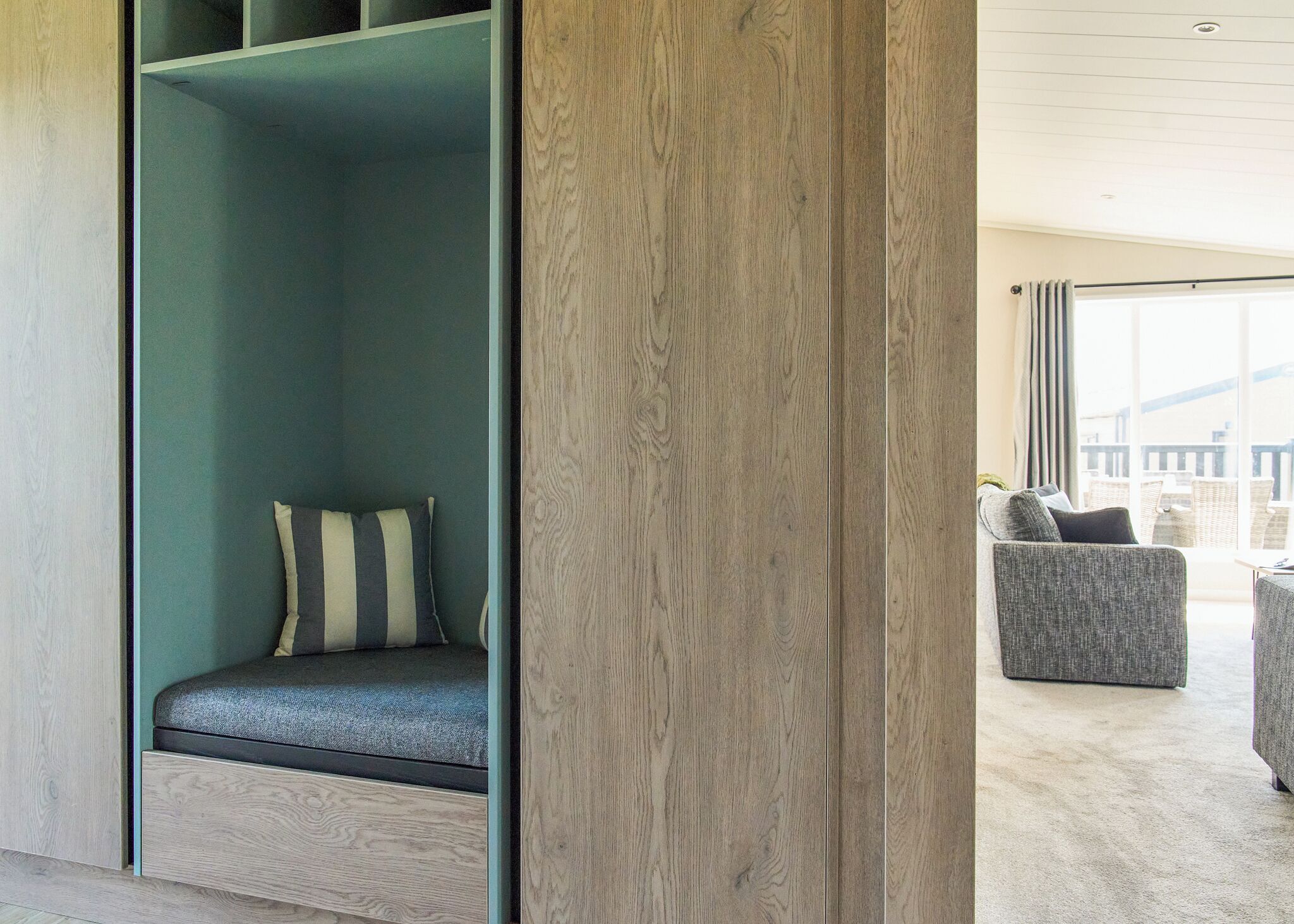 A modern room with a built-in bench, a grey upholstered chair, and a large window offering a view.