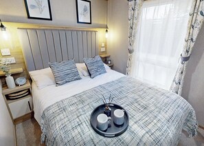 Ein ordentlich eingerichtetes Schlafzimmer mit einem Bett, Nachttischen, einer Ablage mit Tassen und gerahmten Bildern an der Wand.