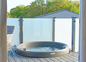 Boblebad på en træterrasse med et hvidt hegn og et hus i baggrunden.