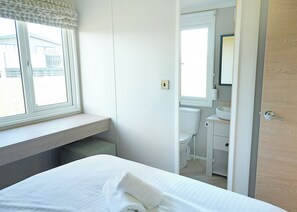 Un dormitorio con cama, ventana, baño con inodoro y lavamanos, y una puerta de madera.
