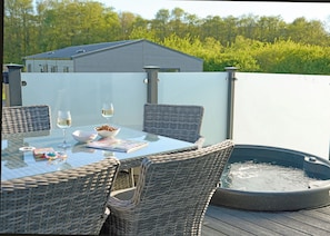Ein Essbereich im Freien mit Korbstühlen, einem Tisch mit Glasplatte, einer Schale mit Snacks, zwei Gläsern Weißwein und einem Whirlpool.