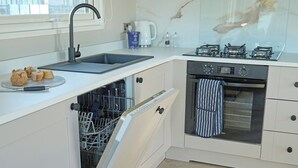 A kitchen with a dishwasher, oven, and a coffee maker on the counter. - Premium Hot Tub 4 bedroom Holiday Home sleeps 8 (Landford, Nr Salisbury)