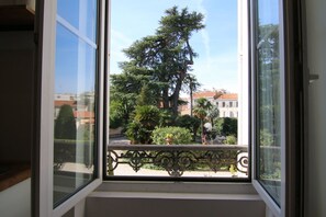 Ein Fenster mit Blick auf einen Balkon, einen großen Baum und Gebäude im Hintergrund.